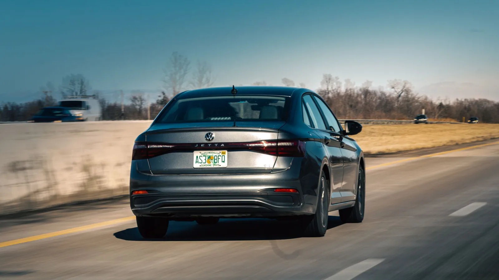 Rear view of a silver Volkswagen Jetta driving on an open highway during the day.