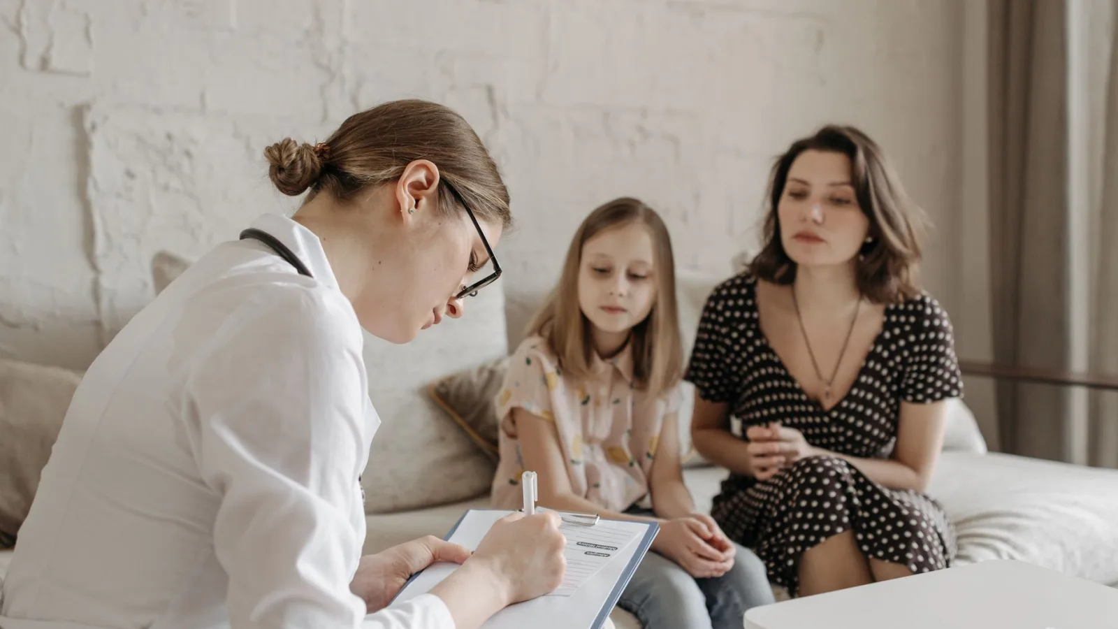 A female doctor consults with a mother and daughter inside a cozy room.