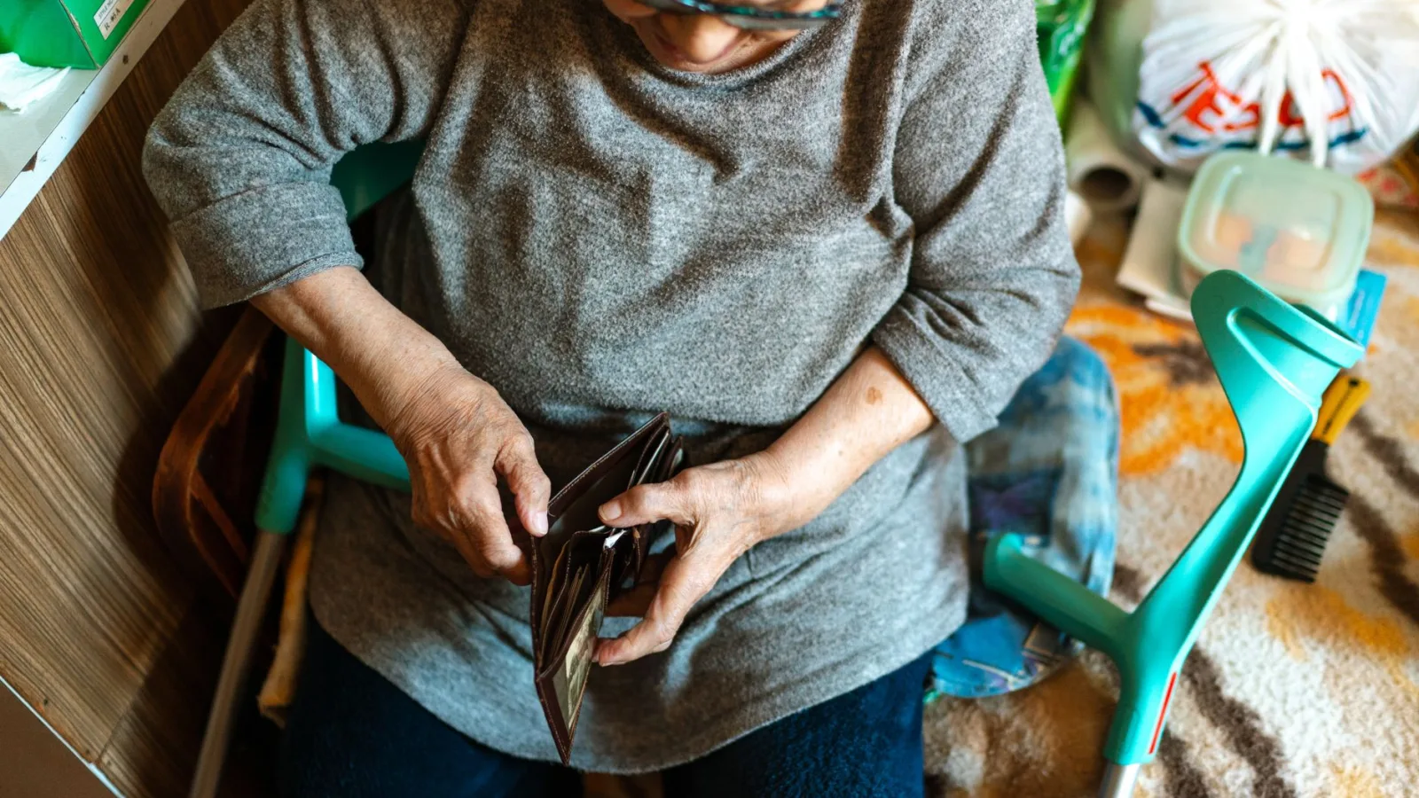 Elderly woman sitting indoors managing her wallet. Home care theme.