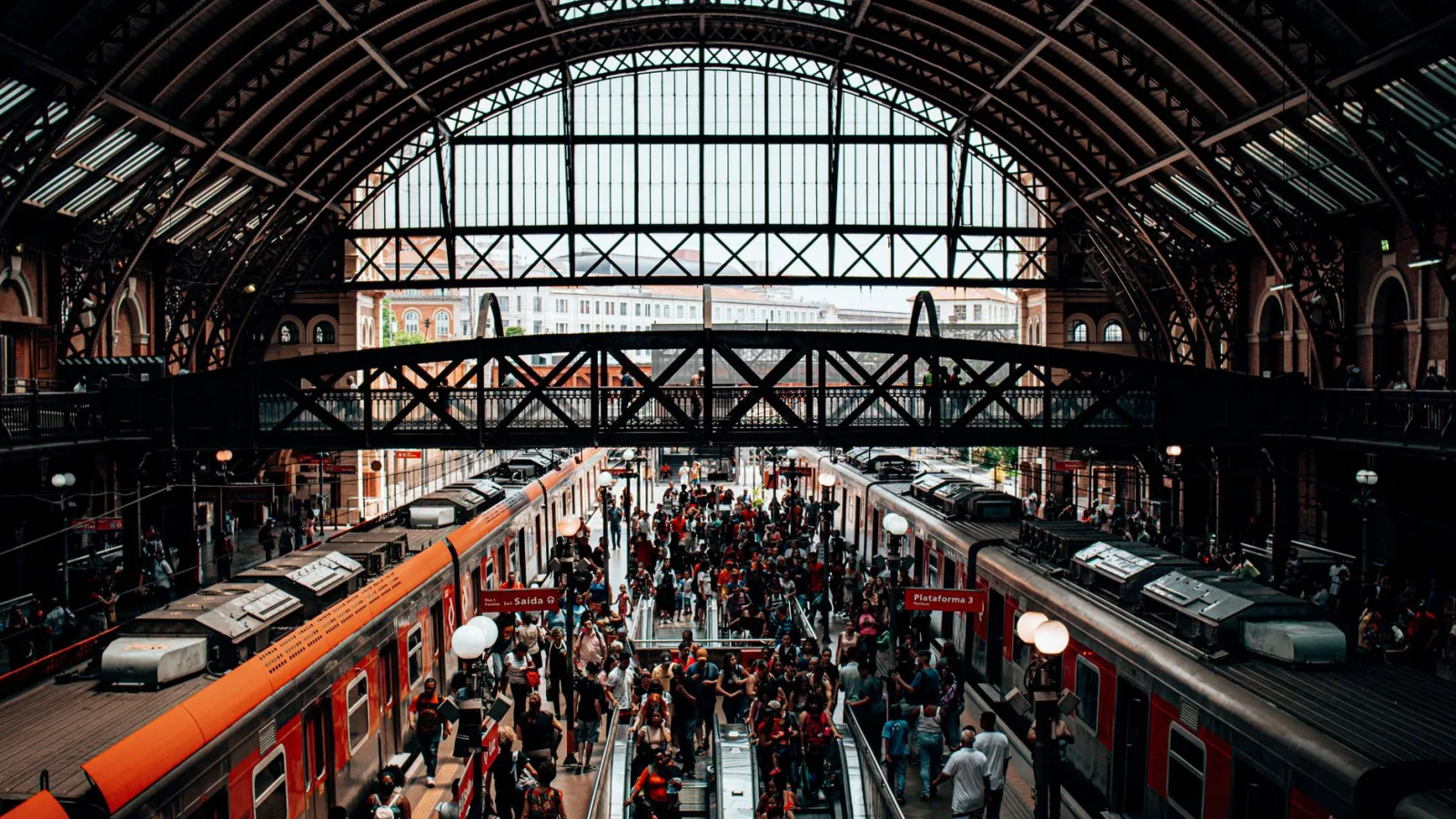A bustling scene of people at a historic train station with arched roof and platforms.