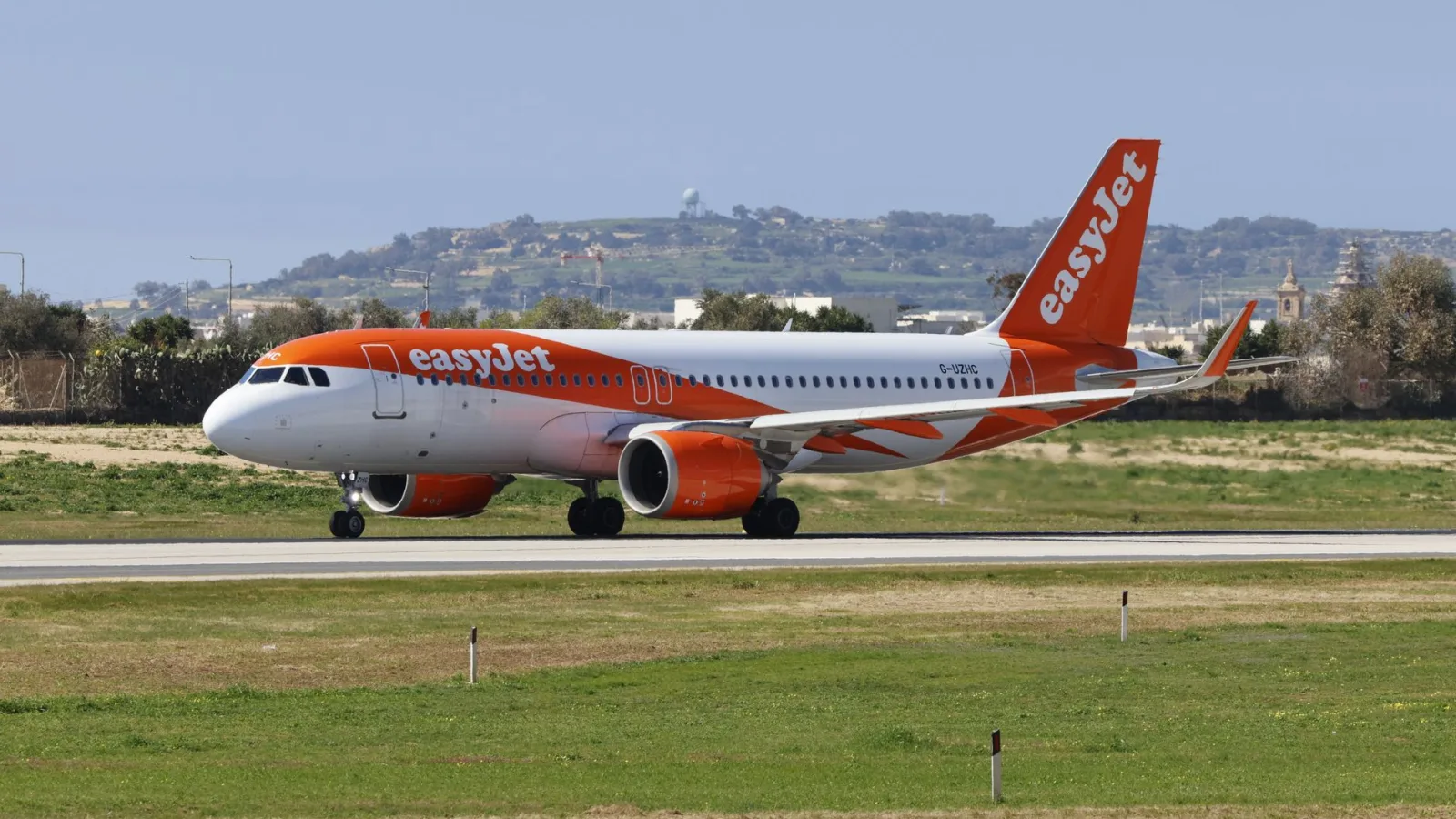 An EasyJet airplane taxiing on the runway at an airport with a scenic background.