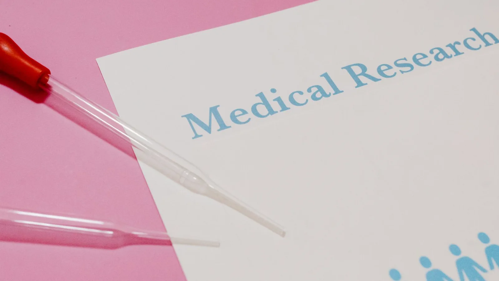 Close-up of a medical research document and pipette on a pink surface, highlighting scientific research and healthcare.