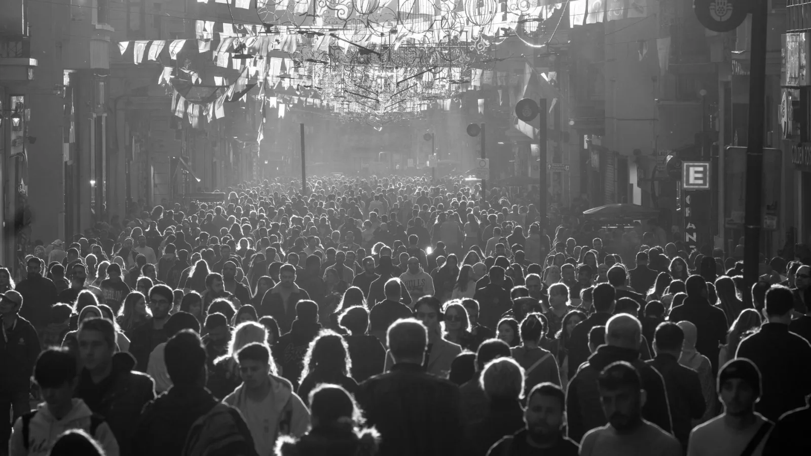 Black and white photo of a busy urban street packed with pedestrians in sunlight.