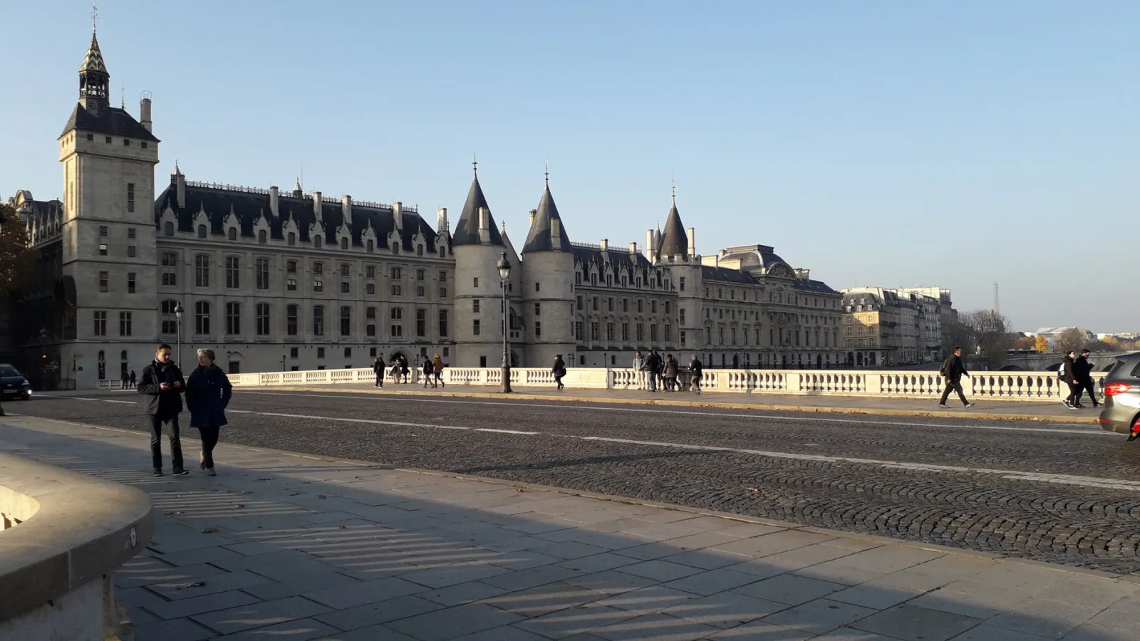 A scenic view of the historic Conciergerie Palace in Paris with people strolling nearby.