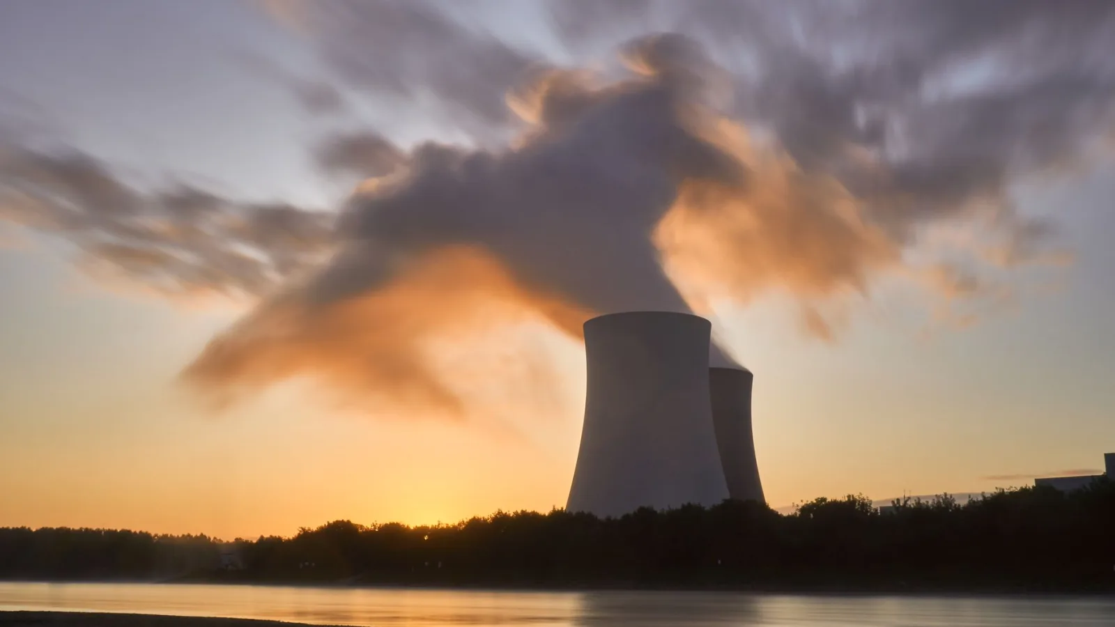 Dramatic image of a nuclear power plant at sunrise with steam rising into a colorful sky.