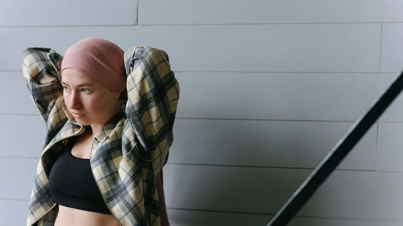 A woman with a headwrap in a casual plaid jacket poses indoors, looking contemplative.