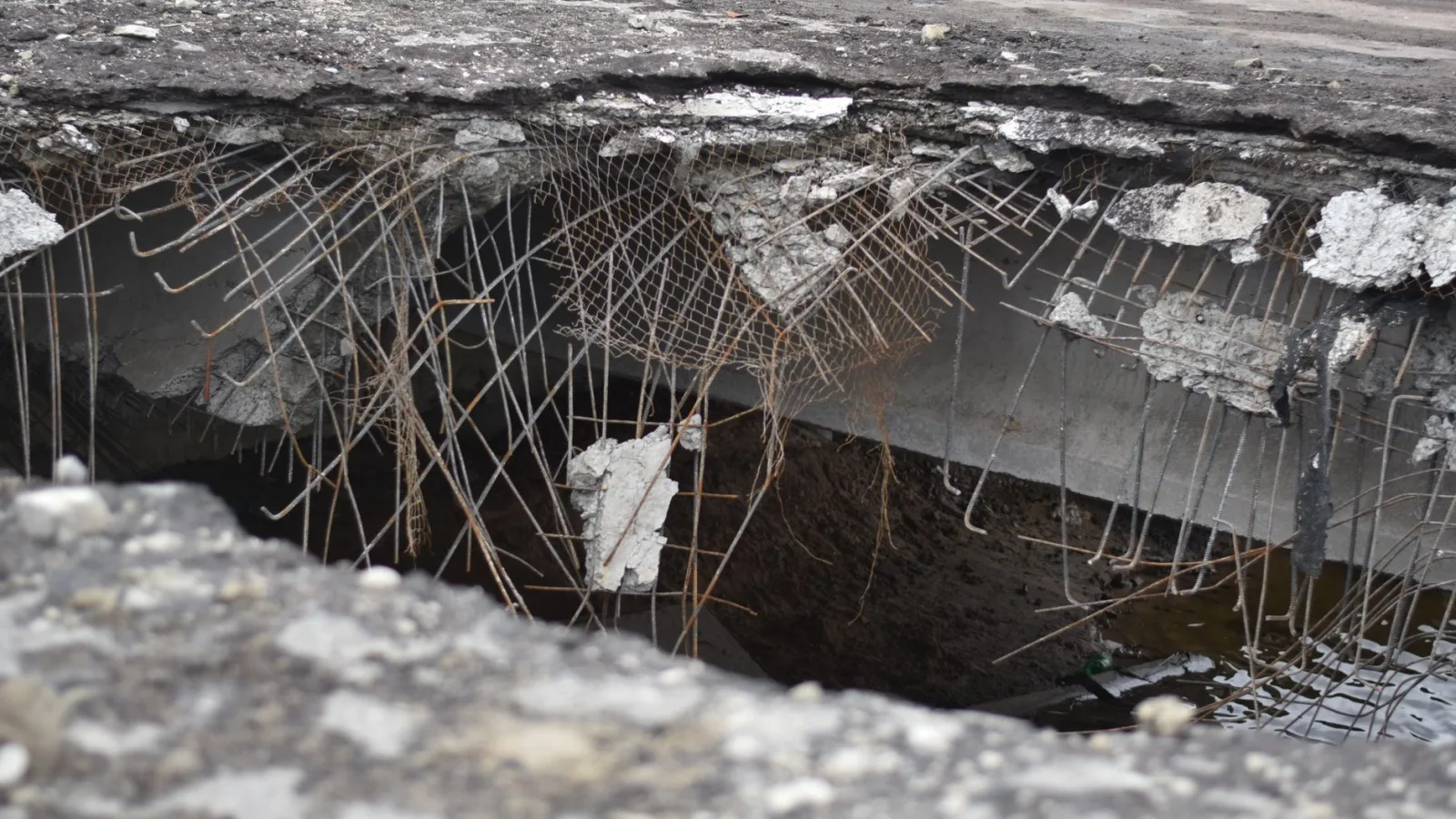 A close-up of a damaged concrete structure with exposed rebar, depicting urban decay.