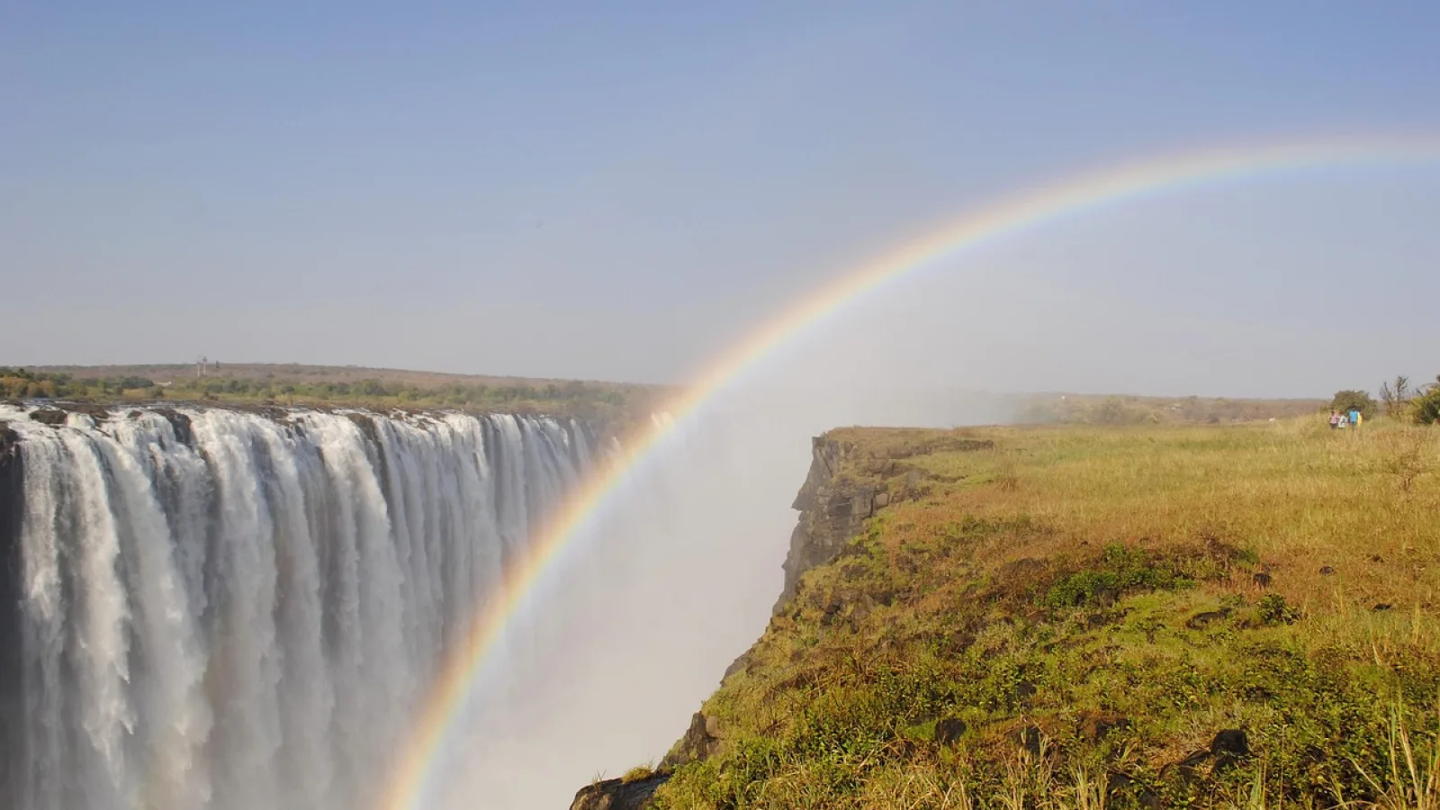 Pale lunar rainbow glowing above Victoria Falls at night amid mist and dark sky